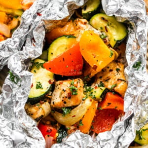 overhead shot of diced chicken, sliced zucchini, and sliced peppers all layered in an aluminum foil packet.
