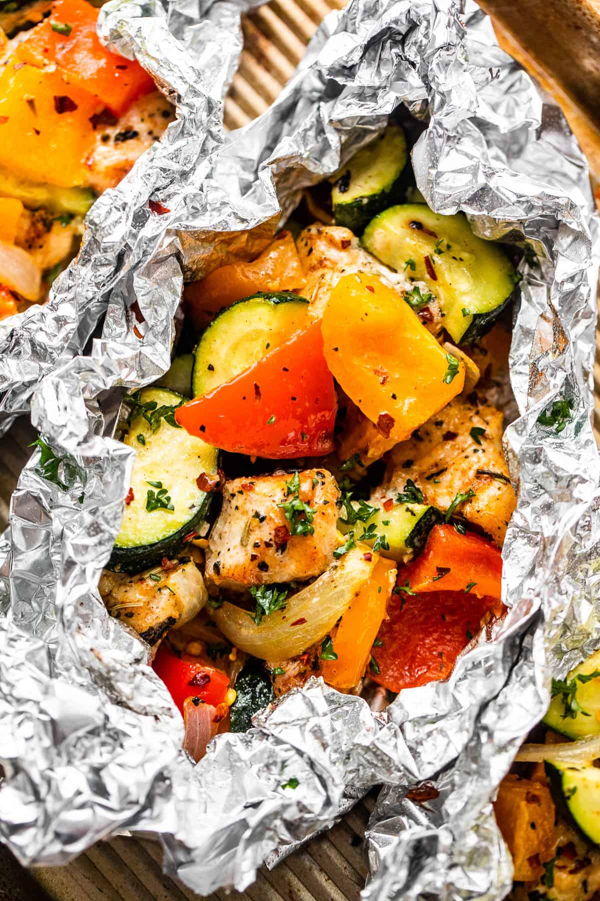 overhead shot of diced chicken, sliced zucchini, and sliced peppers all layered in an aluminum foil packet.
