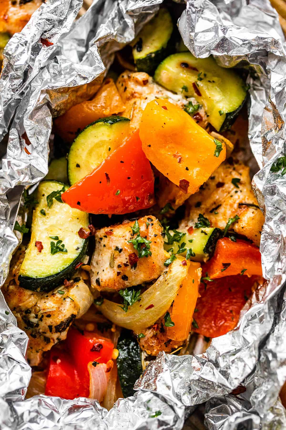 up close shot of diced chicken, sliced zucchini, and sliced peppers all layered in an aluminum foil packet.
