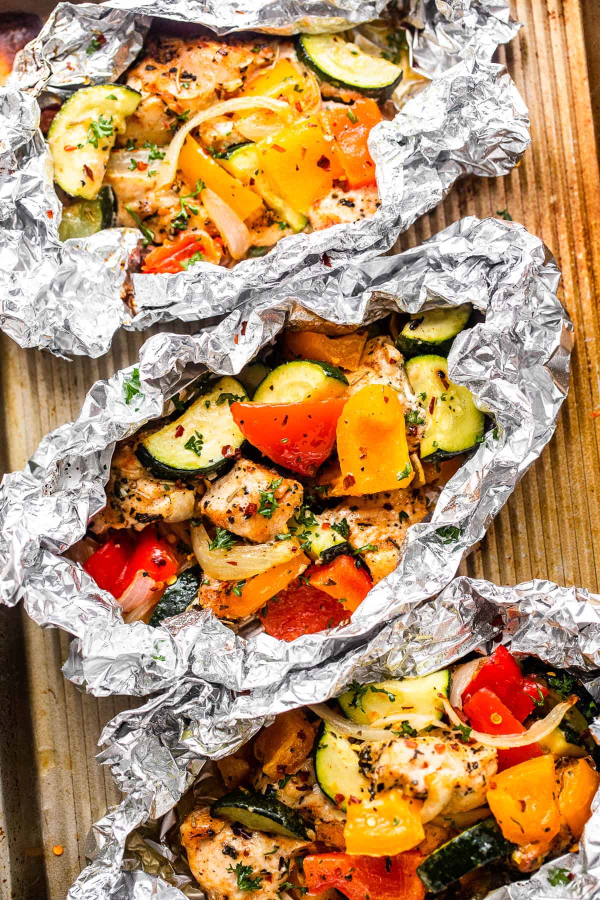 overhead shot of diced chicken, sliced zucchini, and sliced peppers all layered in an aluminum foil packets.