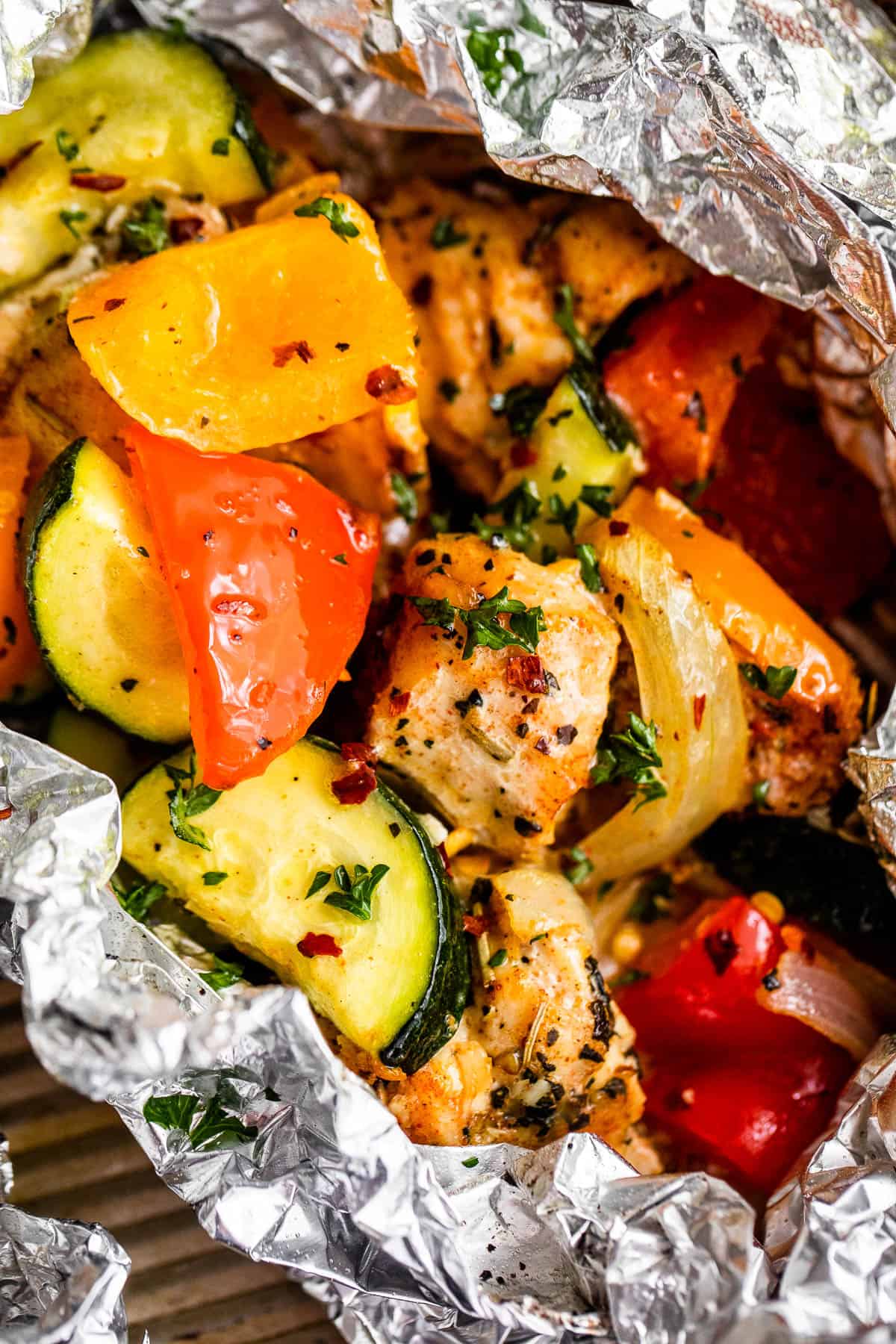 up close shot of diced chicken, sliced zucchini, and sliced peppers all layered in an aluminum foil packet.