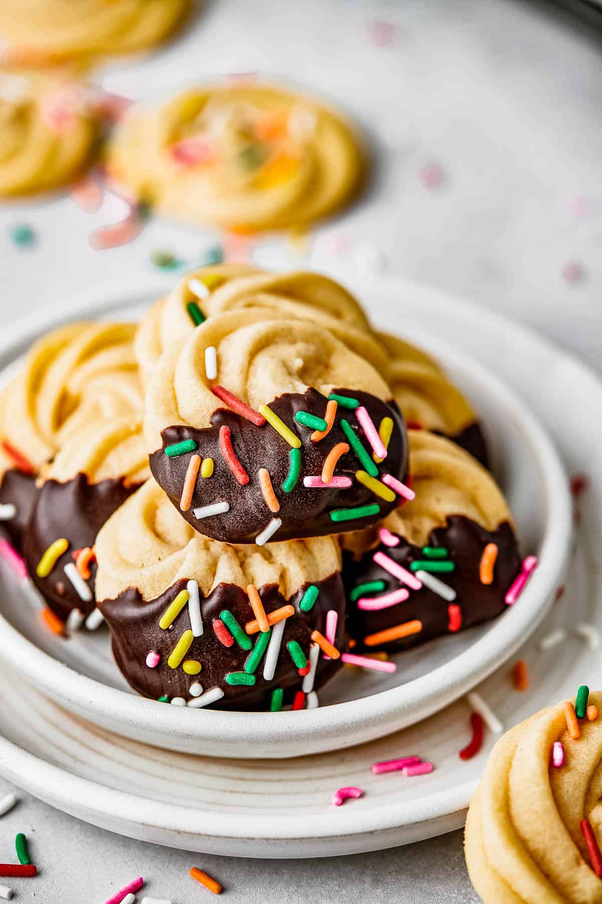 Chocolate iced butter cookies with multicolor sprinkles on a white plate.