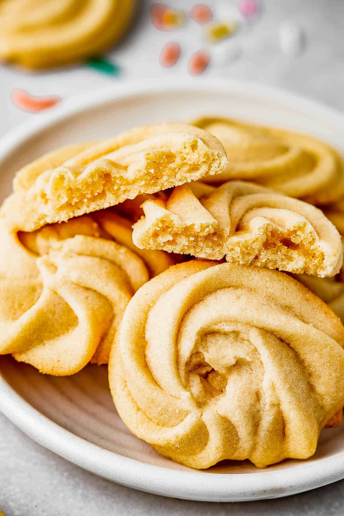 Close-up shot of four butter cookies on a small plate. One of the cookies is broken in half to show texture.