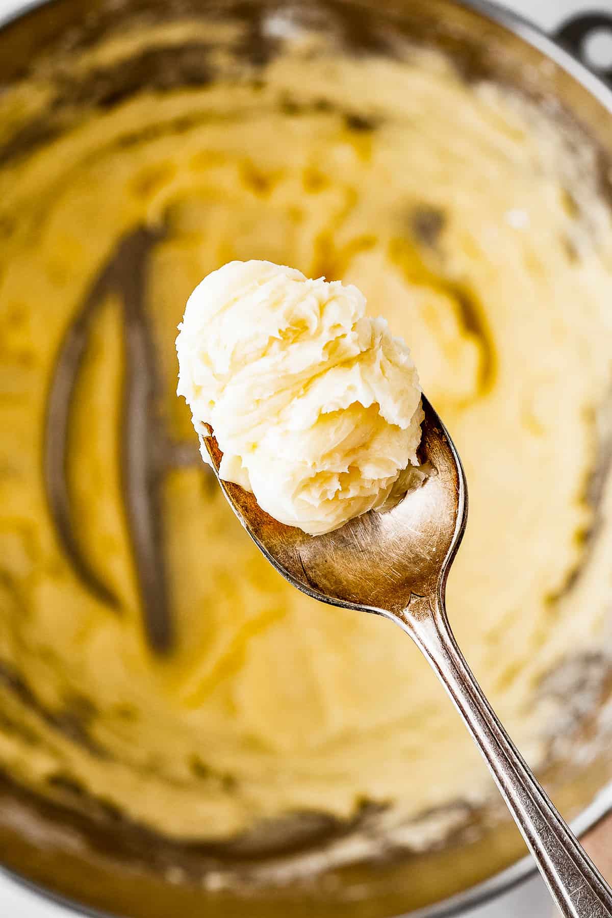 A spoon lifting out a small amount of cookie dough from a mixing bowl.