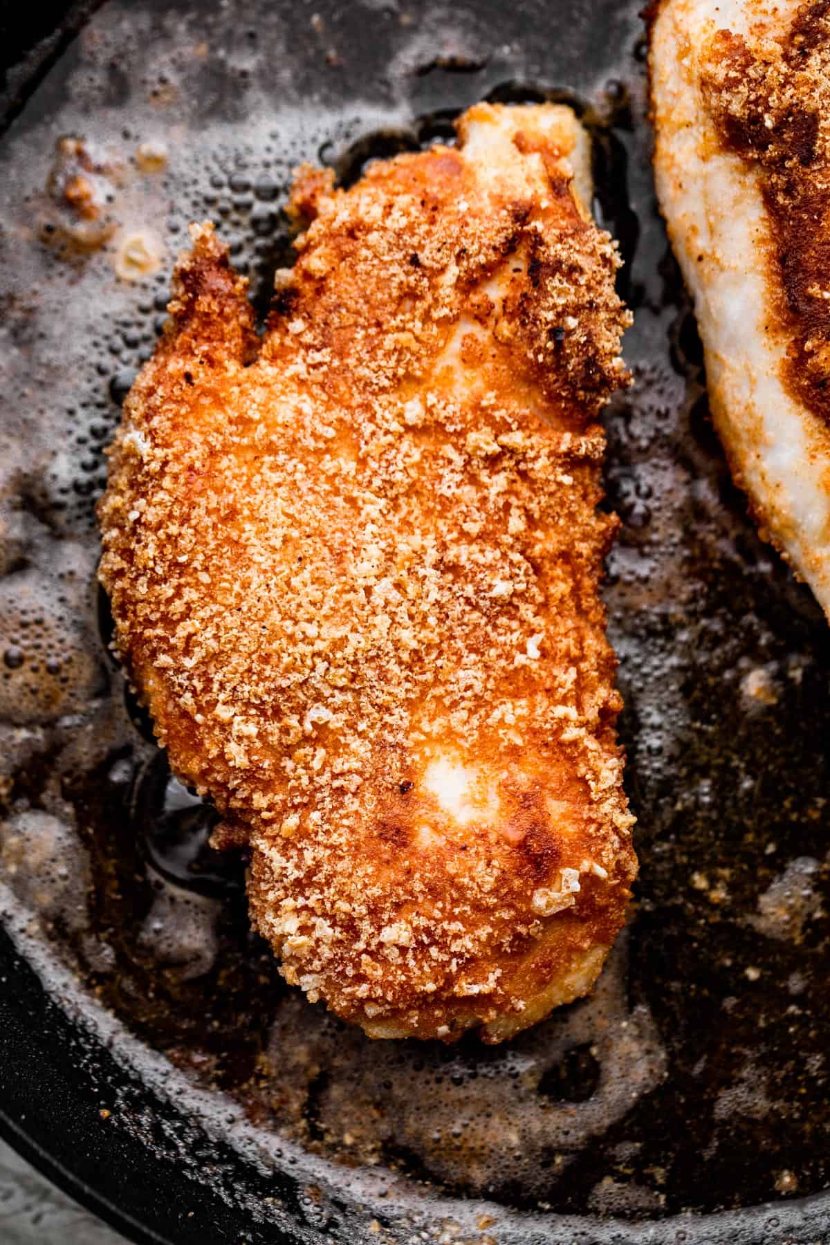 overhead shot of breaded chicken frying in a black skillet.