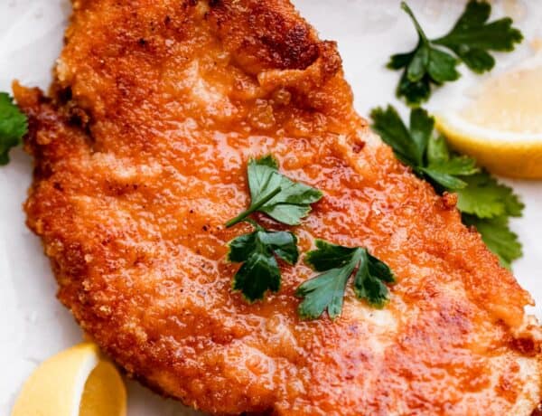 up close shot of chicken schnitzel garnished with parsley and lemon wedges placed around the chicken.