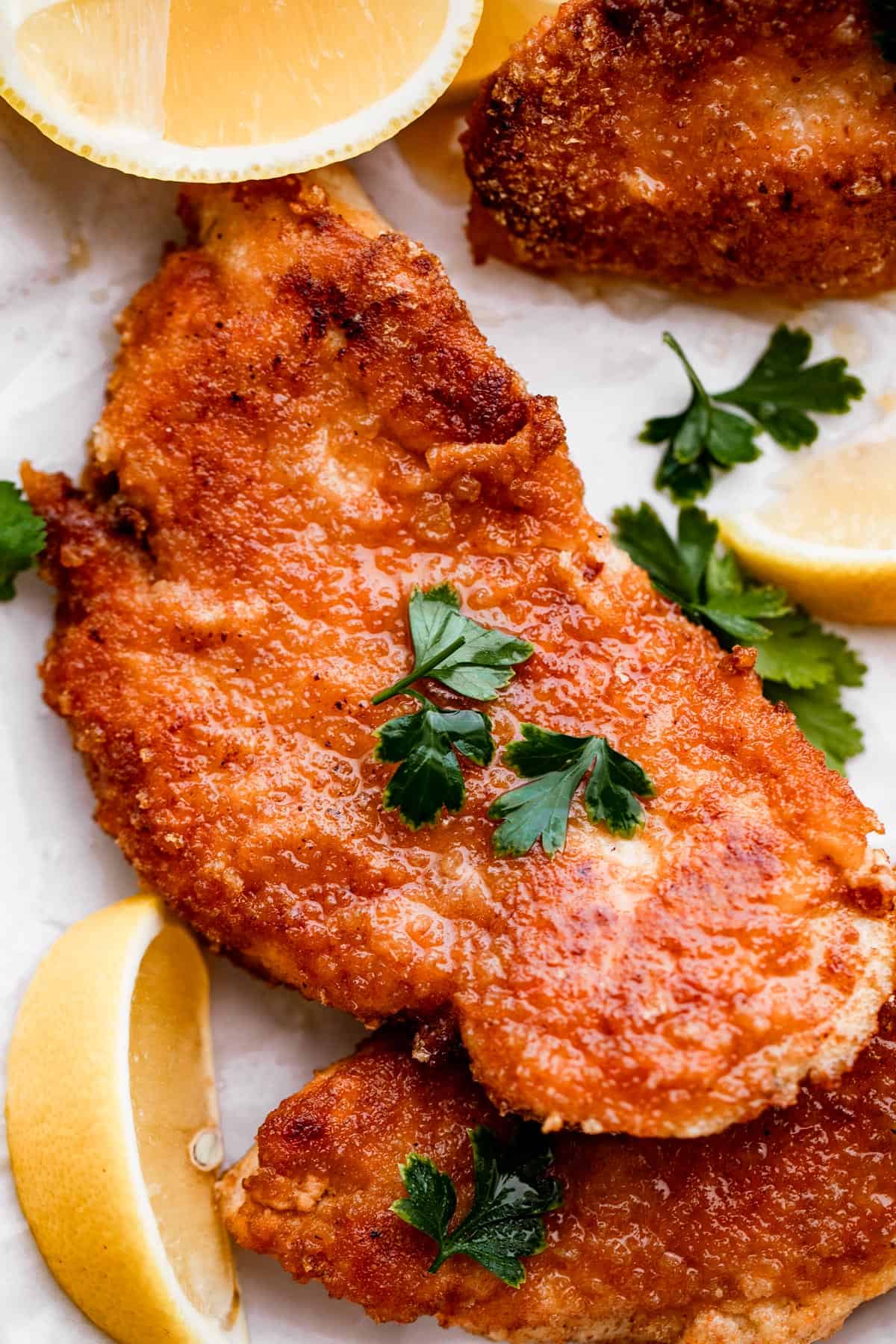 up close shot of chicken schnitzel garnished with parsley and lemon wedges placed around the chicken.