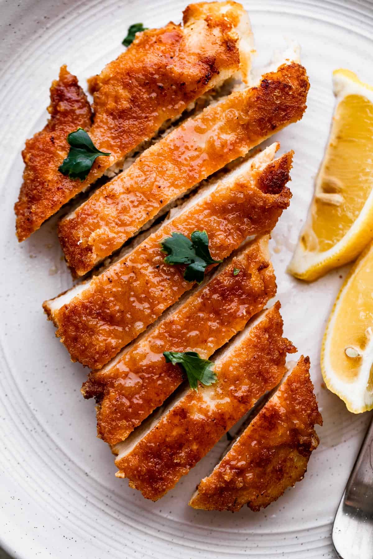overhead shot of chicken schnitzel cut up into slices with lemon wedges placed to the side of the chicken.