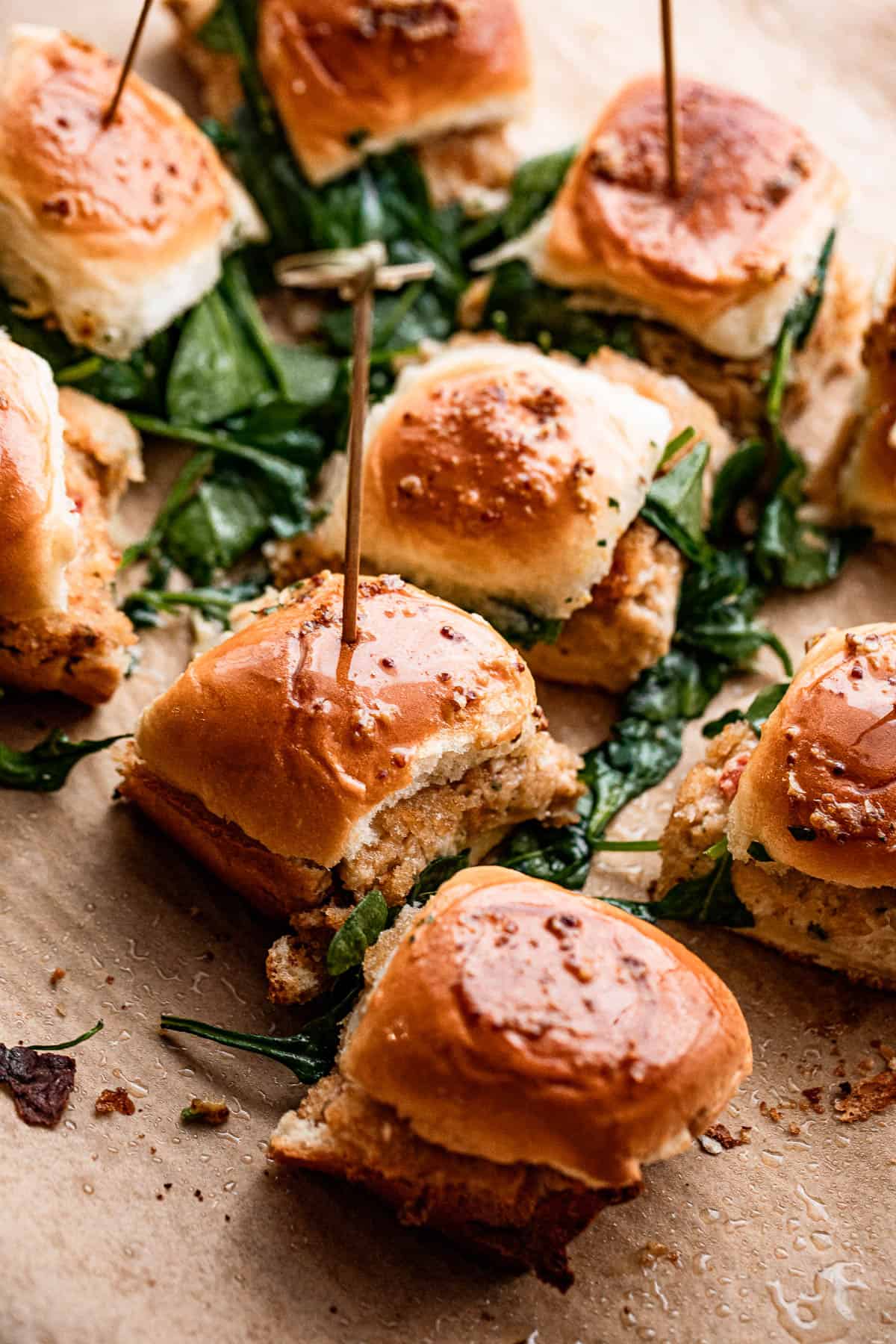 overhead shot of several crab cake sliders with cooked baby spinach scattered around the sliders.