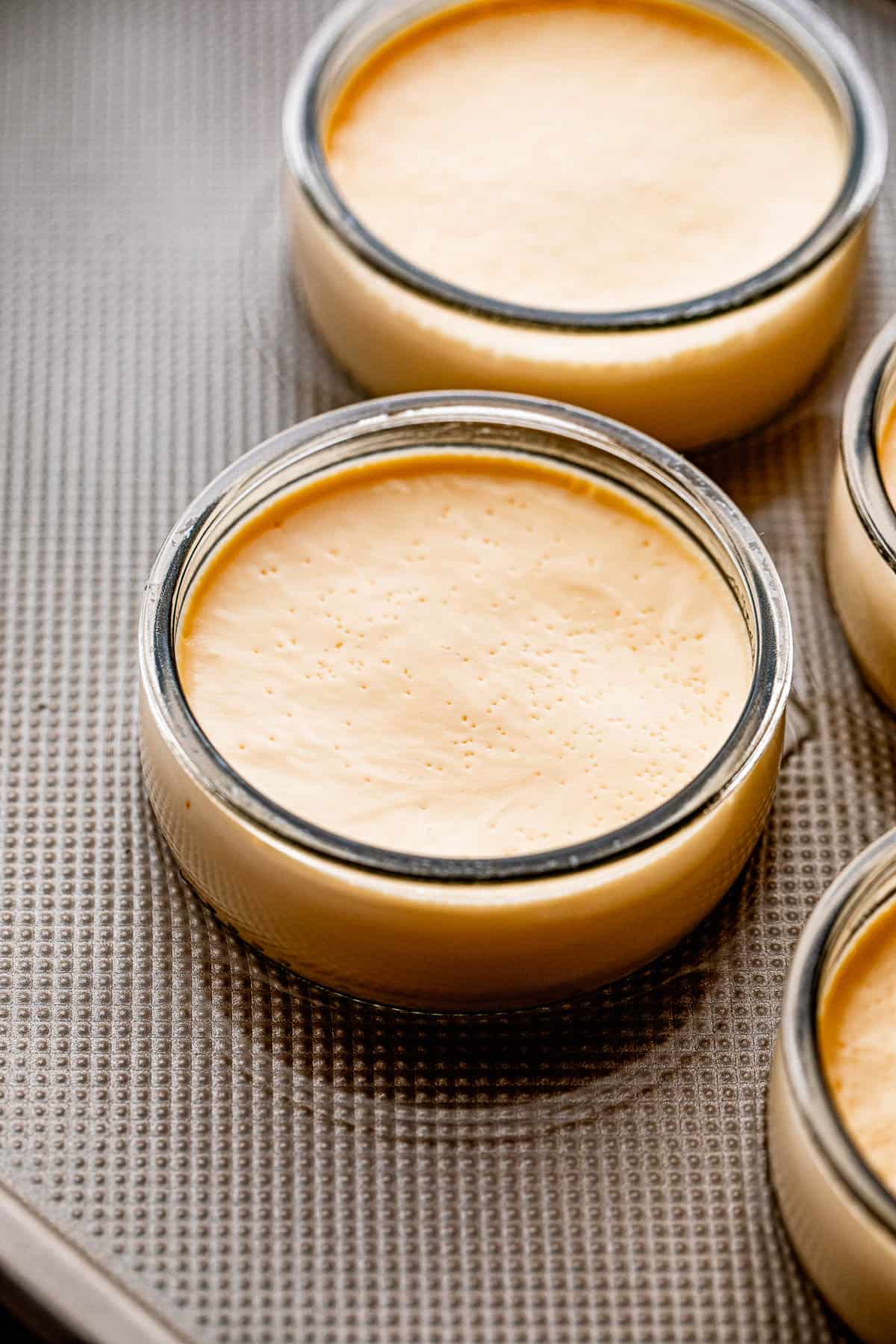 side shot of two jars with creme brulee set on a sheet pan with water.