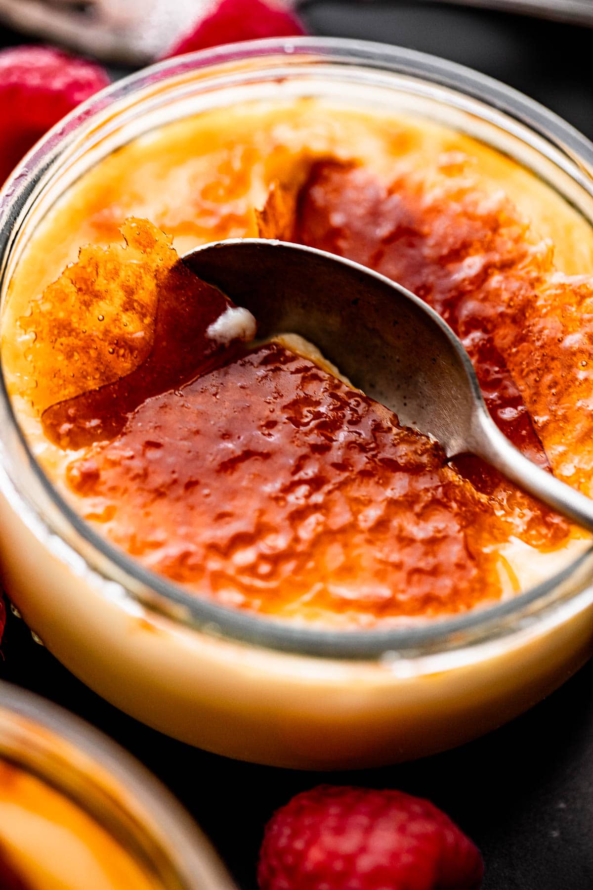 close up side shot of a spoon breaking into the burnt sugar top of creme brulee.