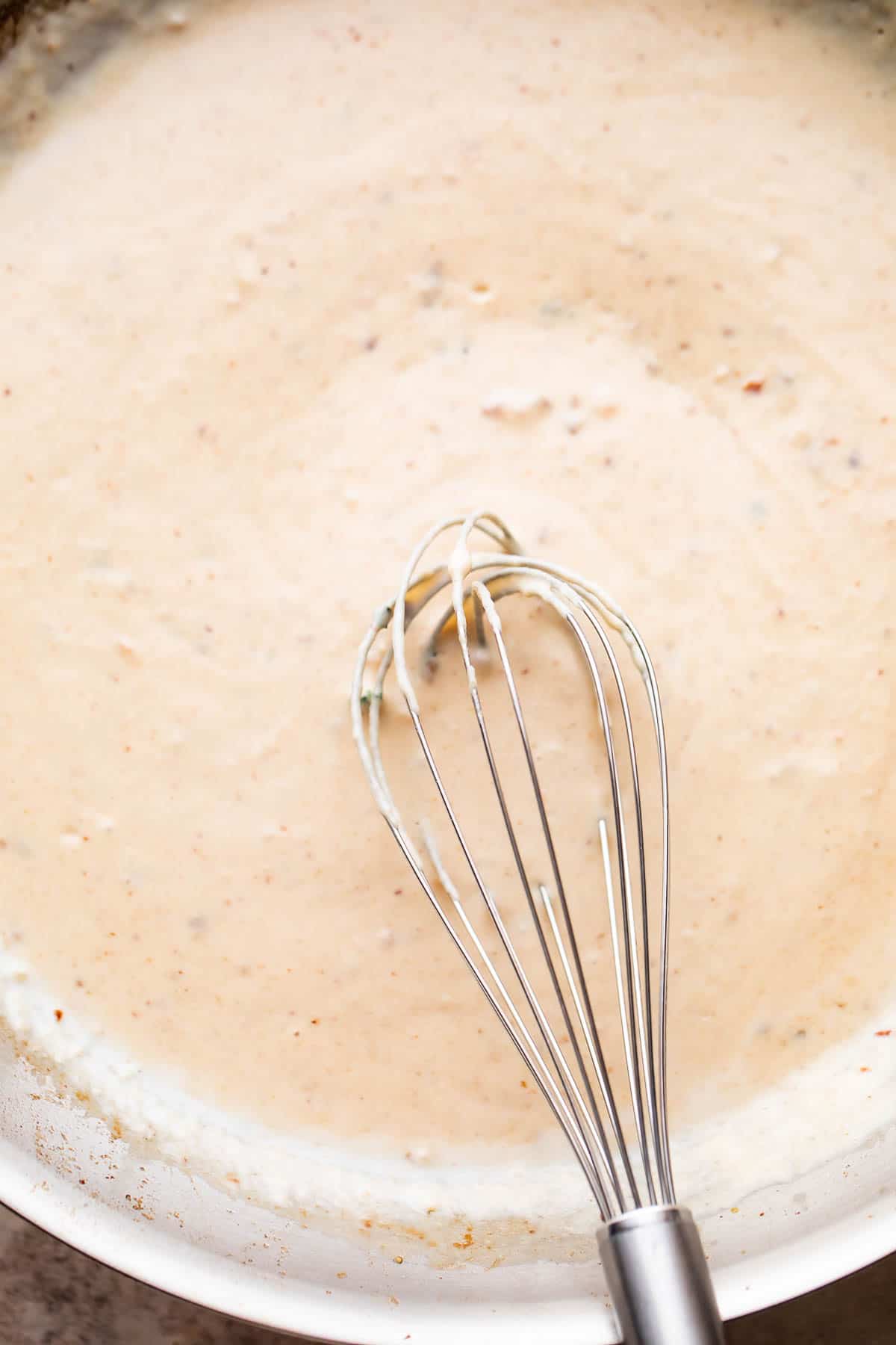 whisking through white cream sauce in a skillet.