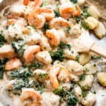 overhead shot of a steel skillet filled with gnocchi, shrimp, and greens.