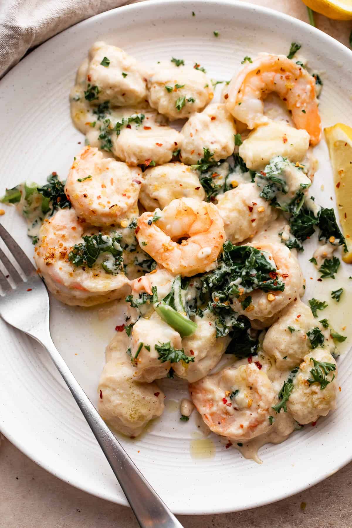 overhead shot of creamy gnocchi with shrimp served on a white plate with a fork placed to the left side on the plate.