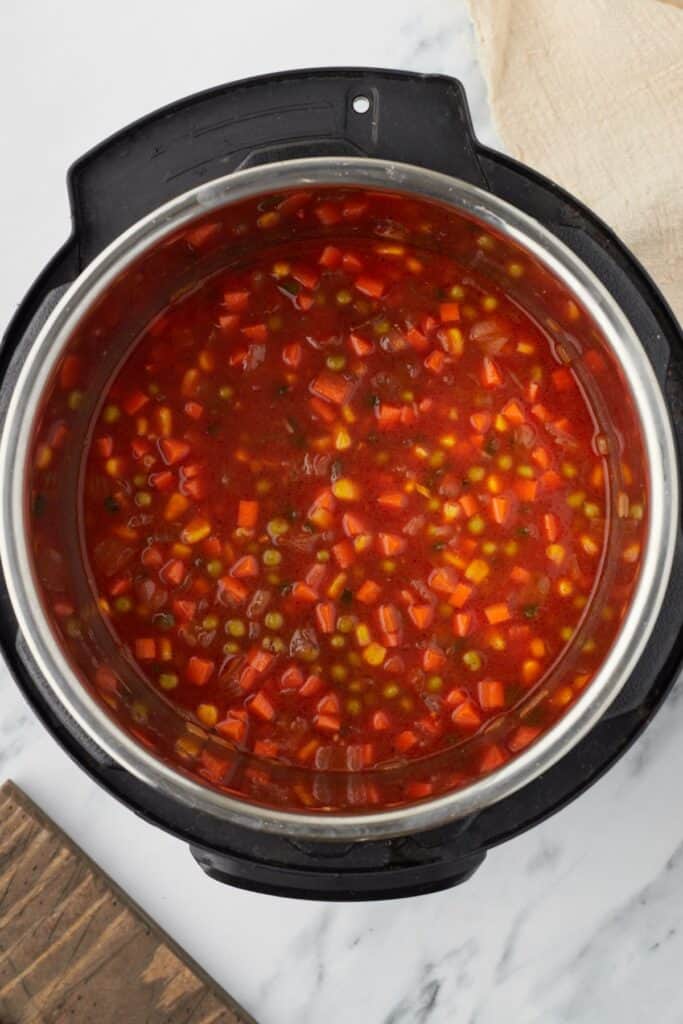 Overhead shot of an Instant Pot, with vegetables and a tomato-based broth inside.