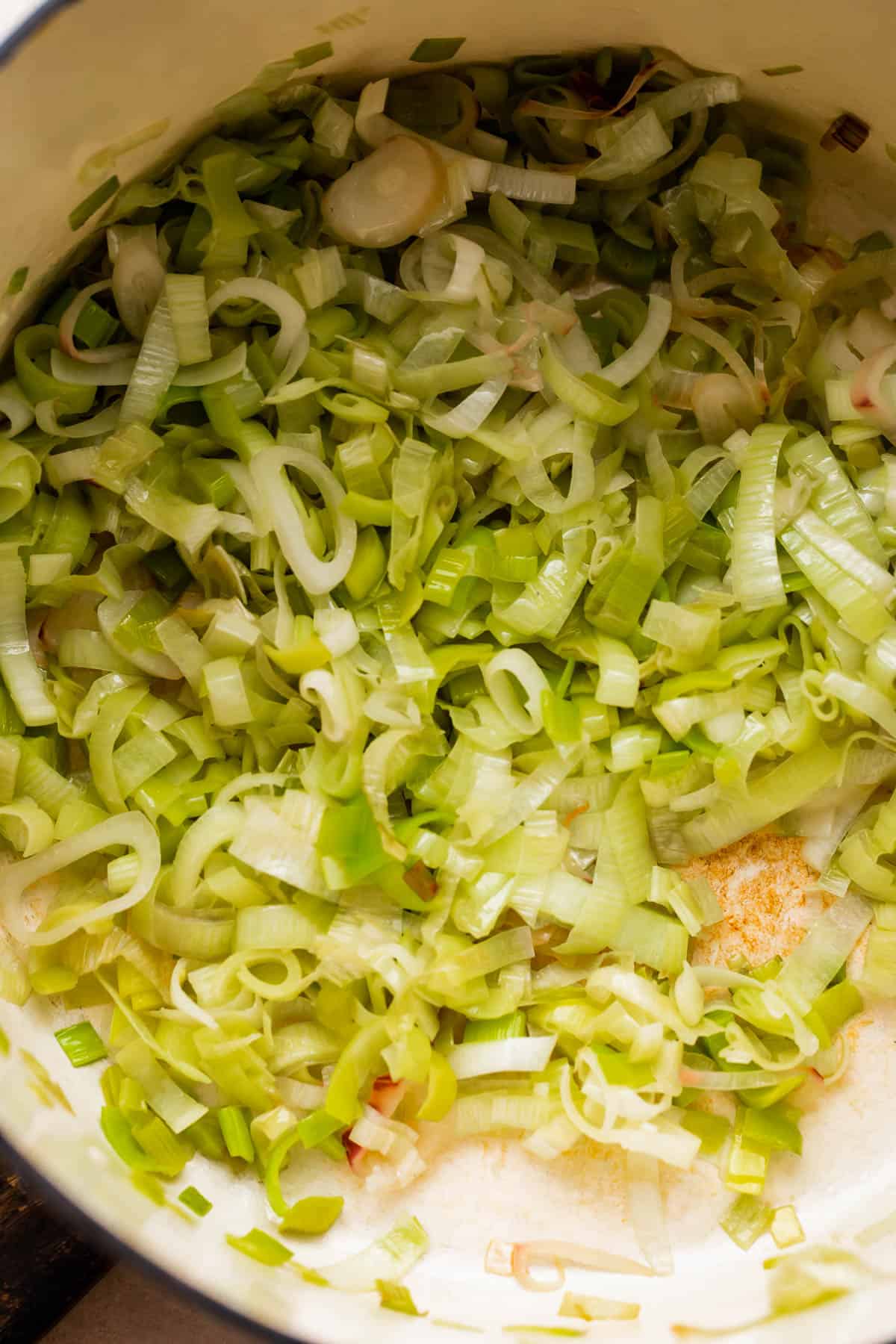 frying sliced leeks in a white dutch oven.