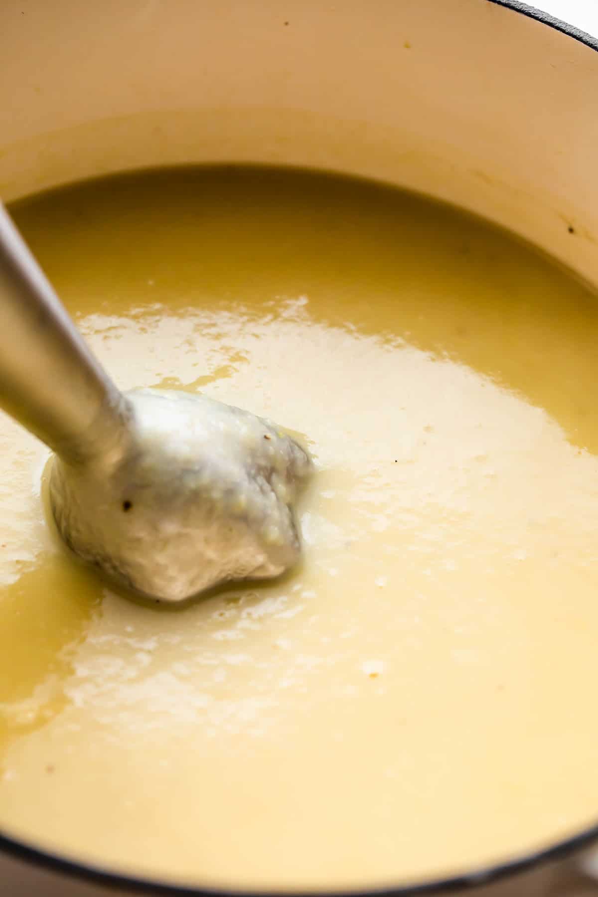 blending a creamy potato and leek soup with a handheld immersion blender.