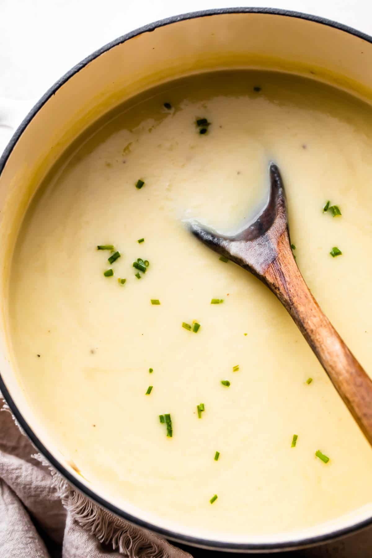 overhead shot of wooden spoon stirring through leek and potato soup in a dutch oven.