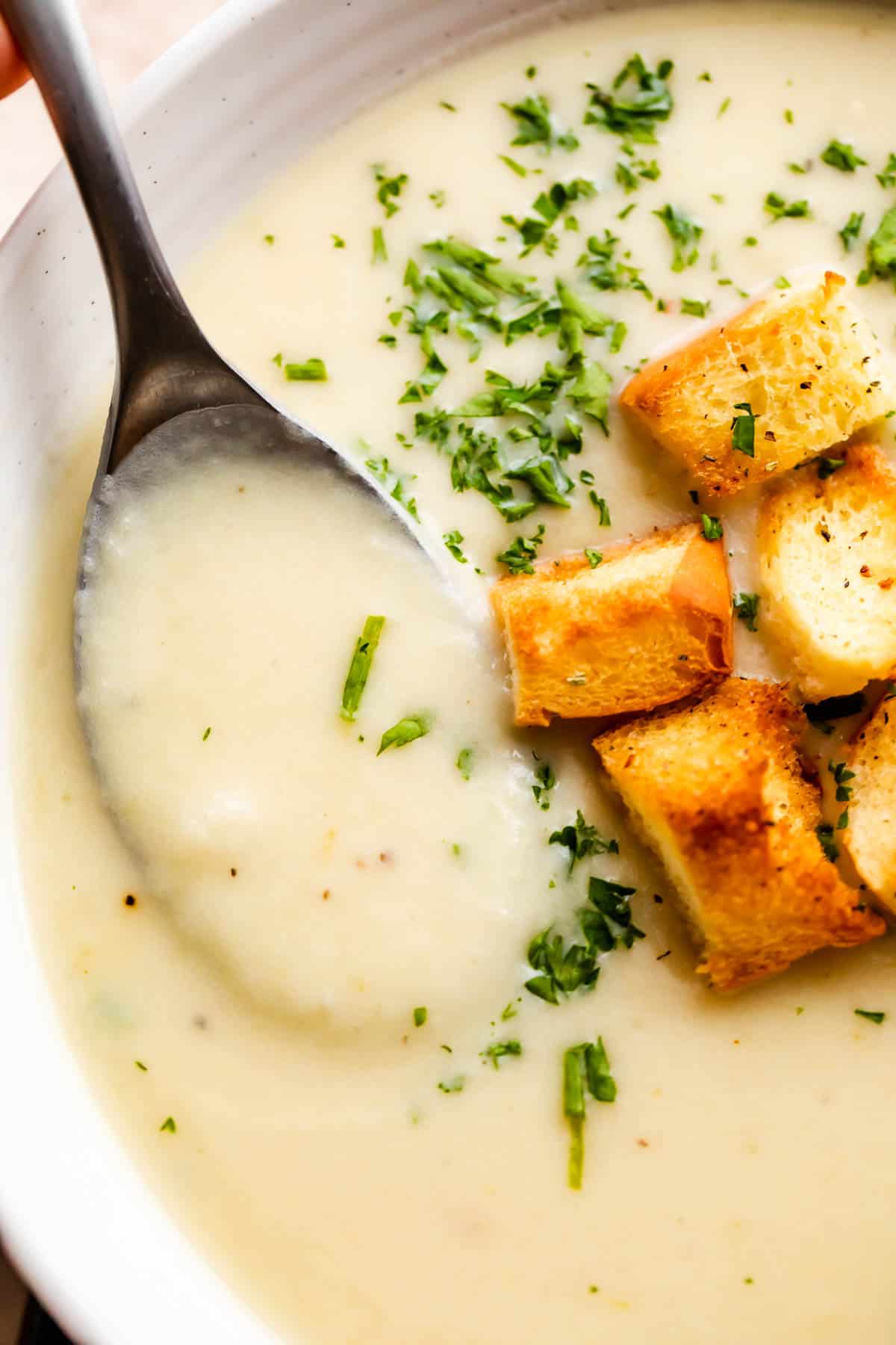 overhead close up shot of leek and potato soup served in a white bowl and garnished with croutons and chopped chives.