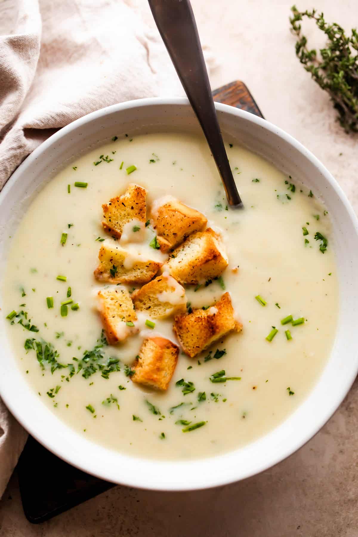 overhead shot of leek and potato soup served in a white bowl with a spoon in the soup, and garnished with croutons and chopped chives.