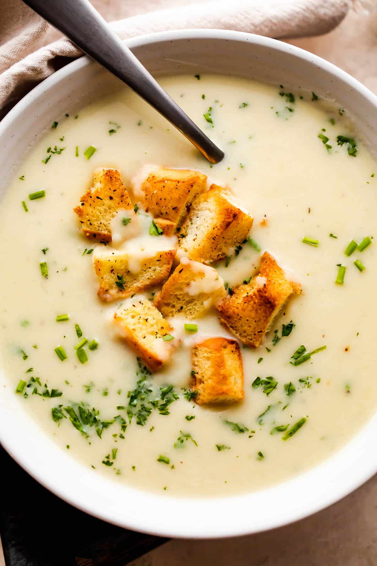 overhead close up shot of leek and potato soup served in a white bowl and garnished with croutons and chopped chives.