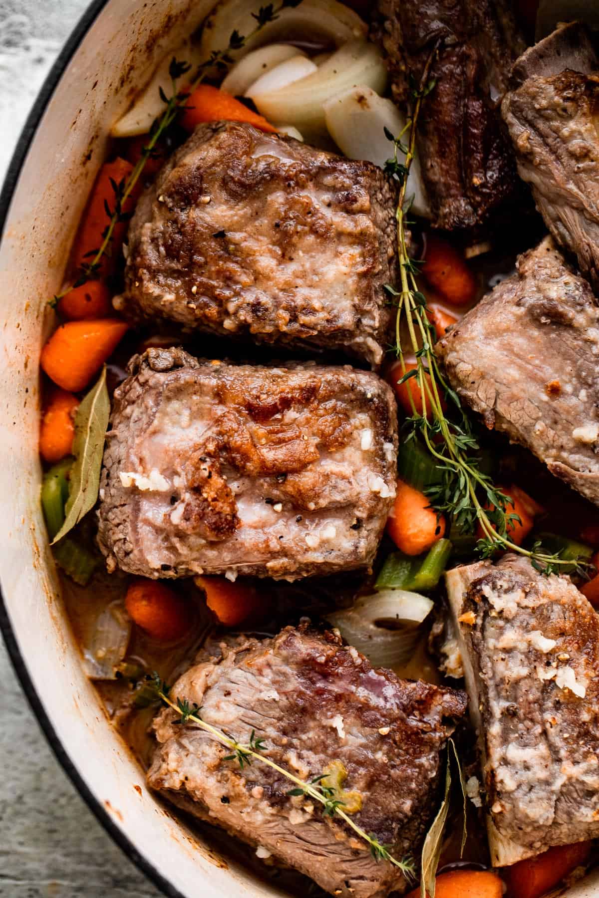 carrots, onions, thyme sprigs, and beef short ribs arranged inside the slow cooker insert.