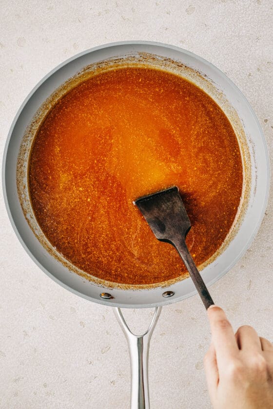 Ham glaze in a saucepan. A woman is stirring the glaze with a spatula.