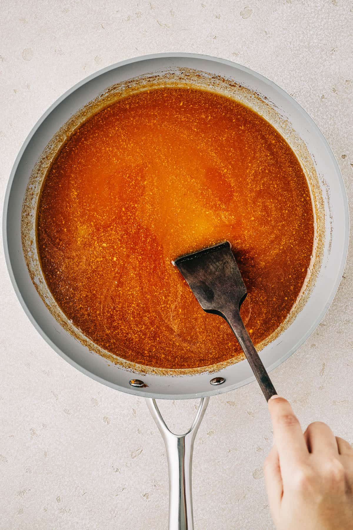 Ham glaze in a saucepan. A woman is stirring the glaze with a spatula.