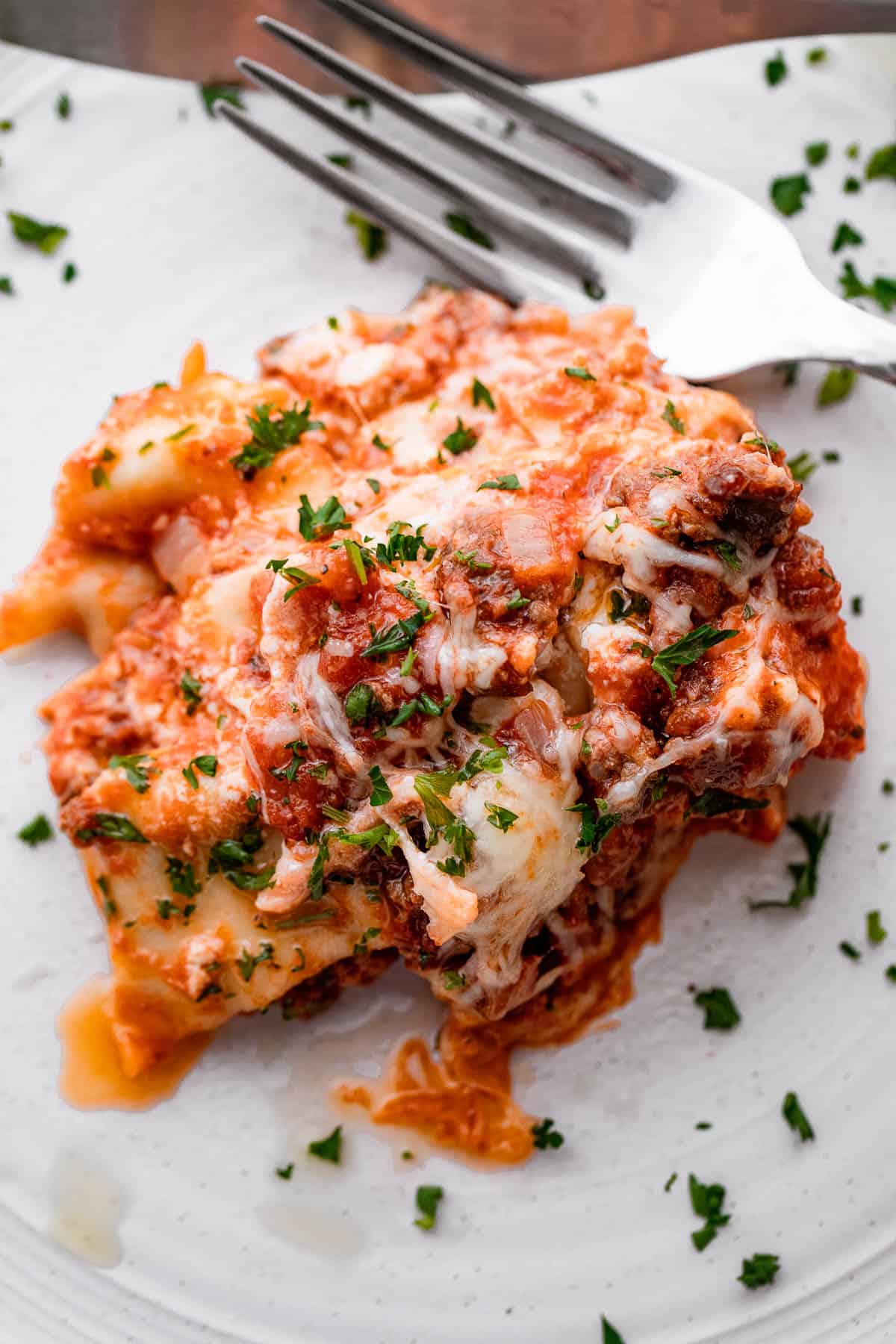 piece of lasagna served on a white plate with a fork placed to the side of it.