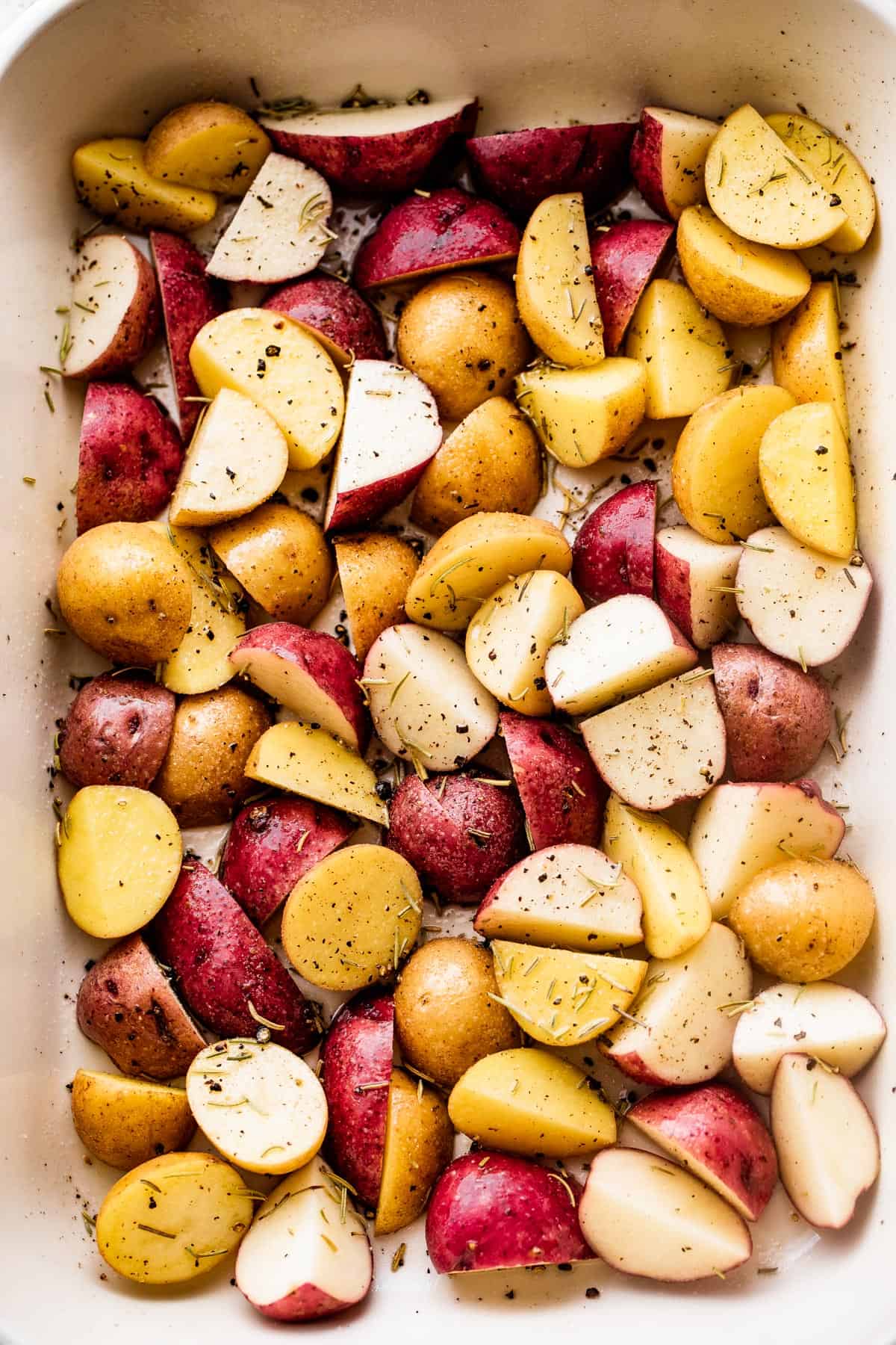 quartered and colorful baby potatoes arranged in a baking dish and seasoned with dried herbs
