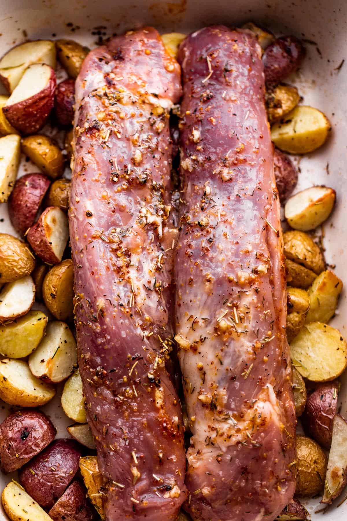 two raw pork tenderloins set over a bed of baby potatoes.