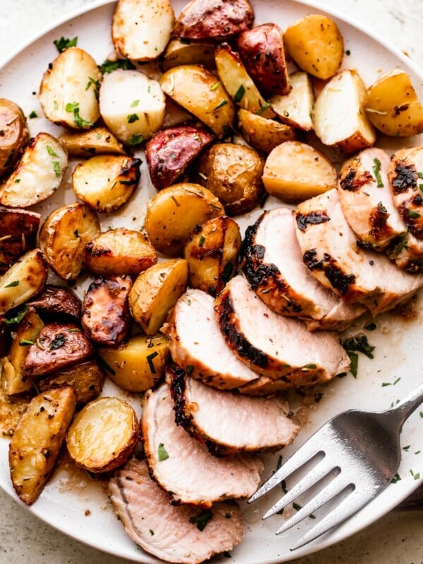 overhead shot of a serving plate with sliced roast pork tenderloin served with colored baby potatoes