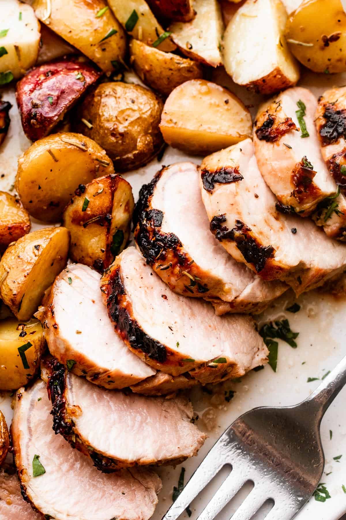close up shot of sliced roast pork tenderloin served with colored baby potatoes