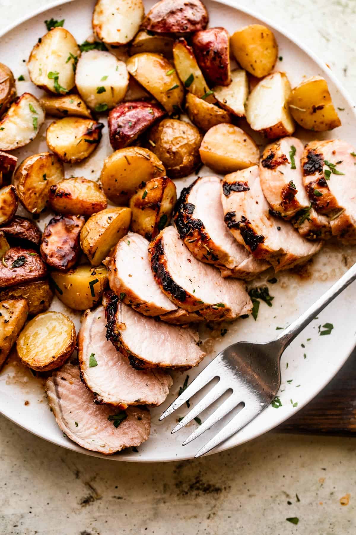 overhead shot of a serving plate with sliced roast pork tenderloin served with colored baby potatoes