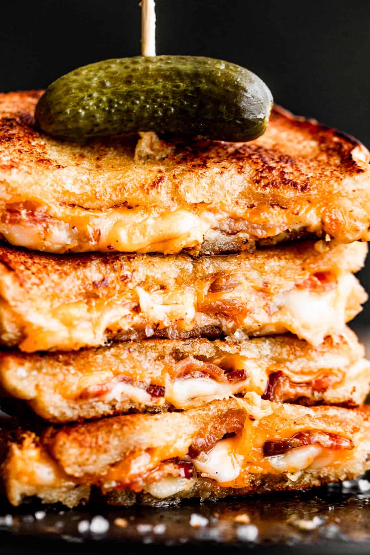 stack of grilled cheese sandwiches topped with a pickle and a long toothpick going through the sandwiches, from top to bottom