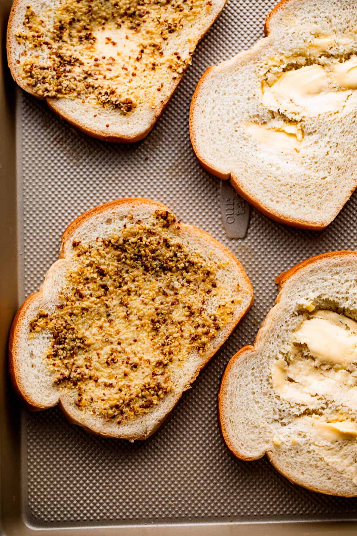 four slices of bread topped with dijon mustard and mayonnaise.