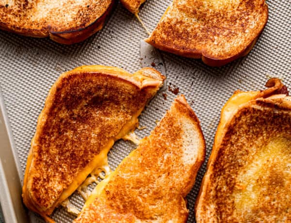 four baked grilled cheese sandwiches set on a baking sheet and diagonally cut in half.