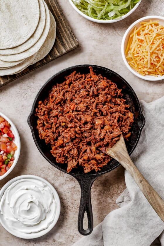 wooden spoon stirring through a skillet full of cooked meat for tacos.