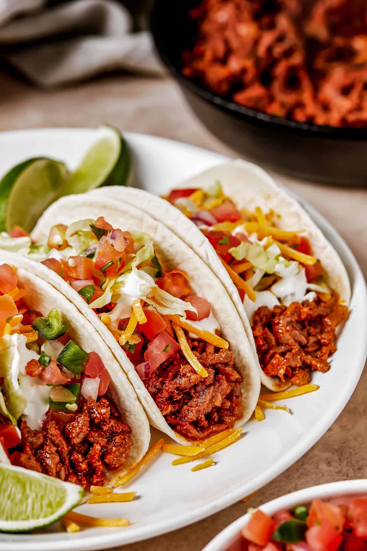 Three soft tacos on a plate with lime wedges.