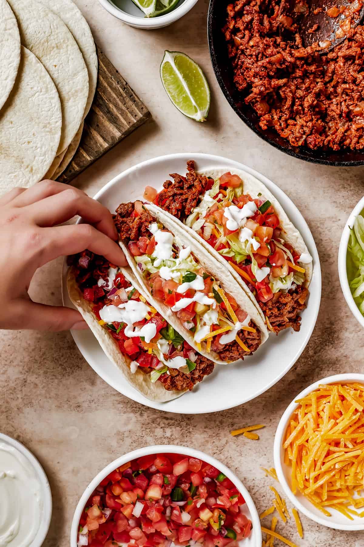A woman's hand lifts a soft taco off of a plate.
