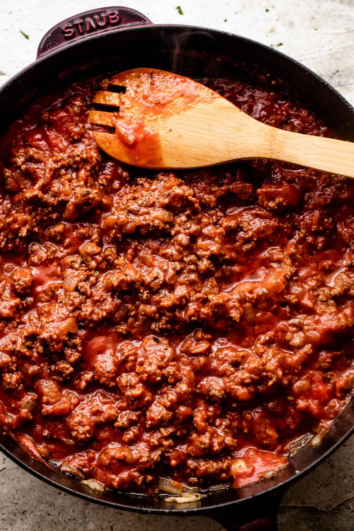 wooden spoon stirring through ground beef that's cooking in a black skillet.