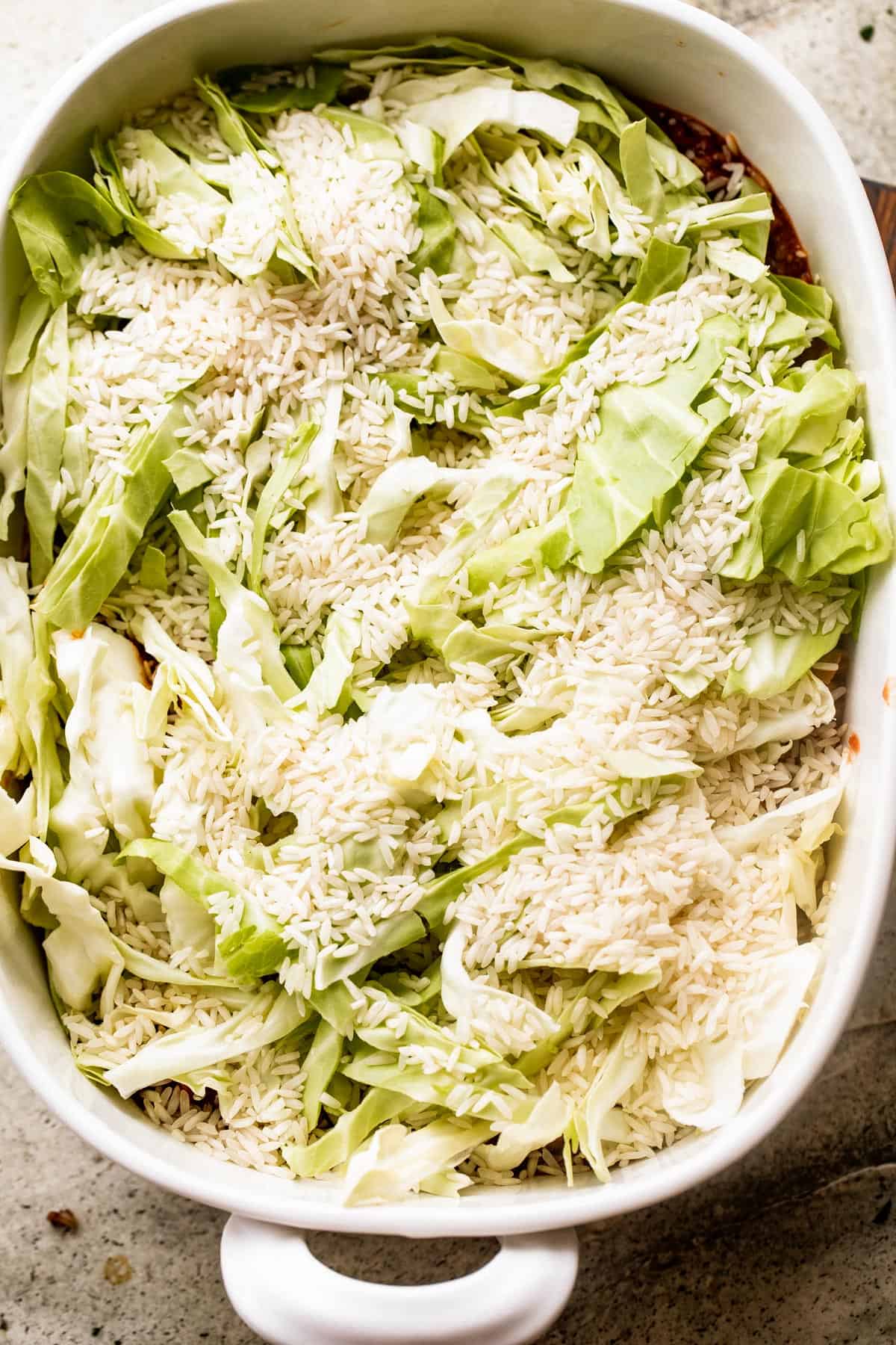 overhead shot of chopped cabbage and dry rice inside a white baking dish