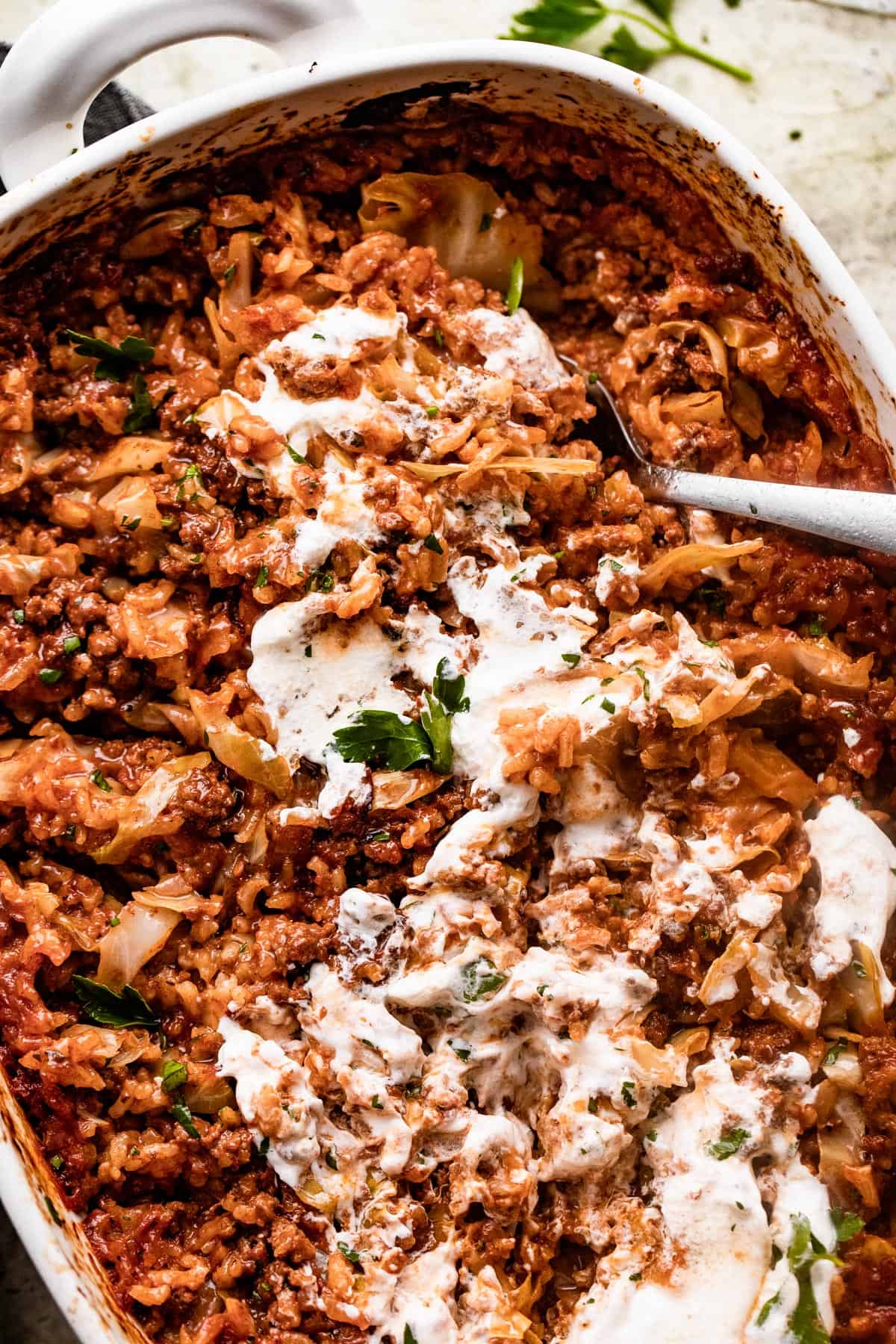 overhead shot of Cabbage Roll Casserole in a white baking dish, and the casserole is smothered with sour cream on top.