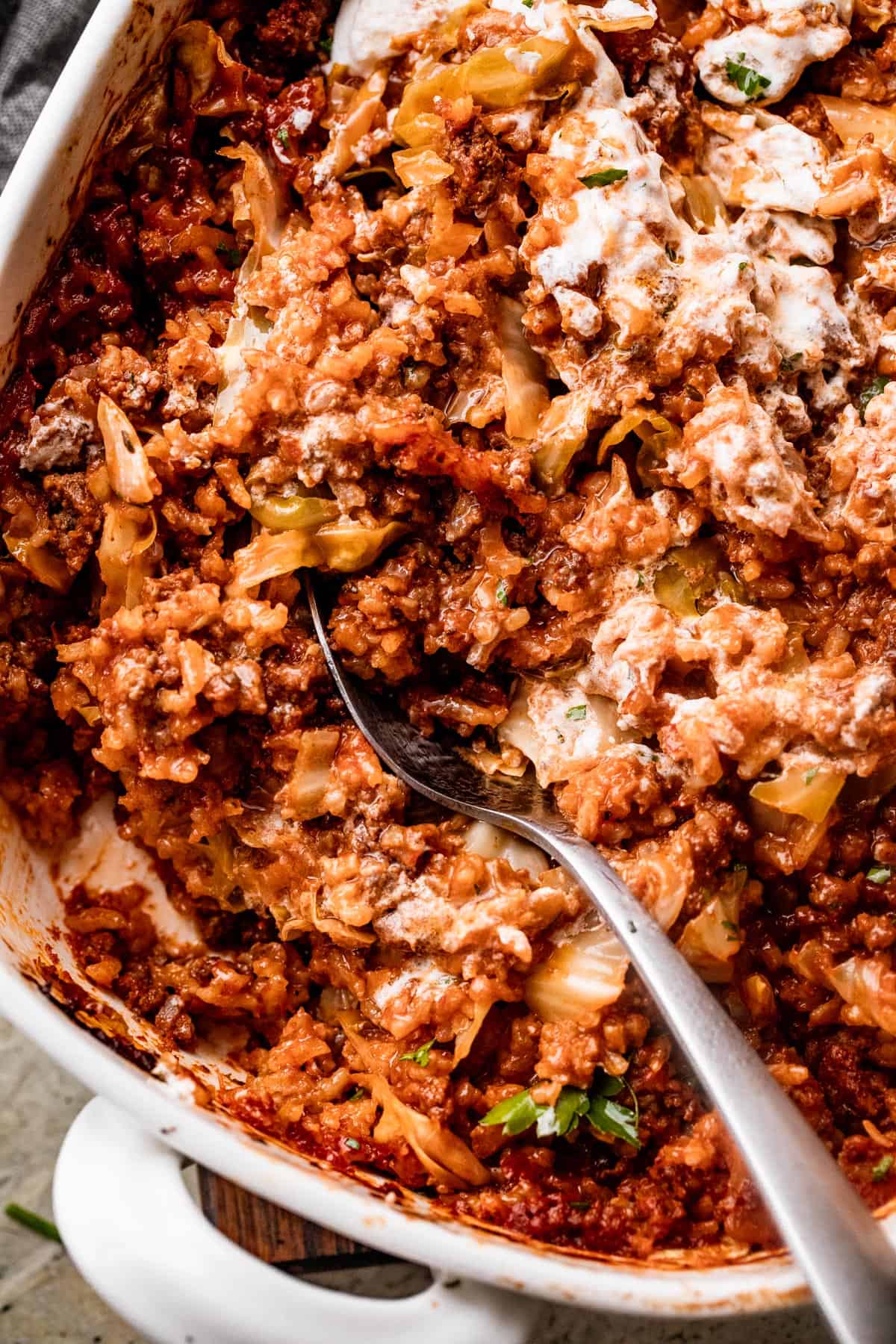long spoon stirring through Cabbage Roll Casserole in a white baking dish.