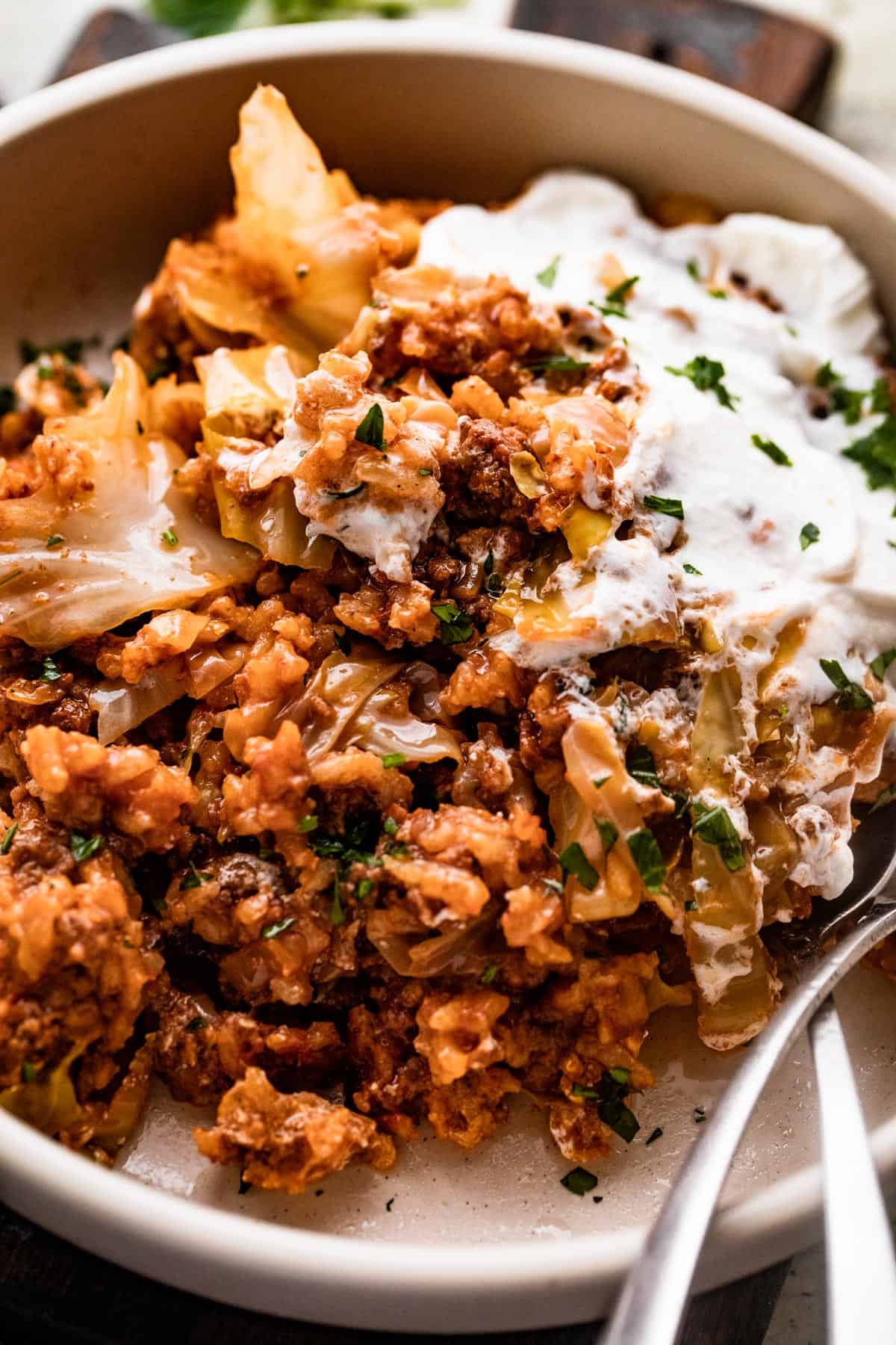 Cabbage Roll Casserole served in a bowl, topped with sour cream, and two utensils placed inside the bowl.
