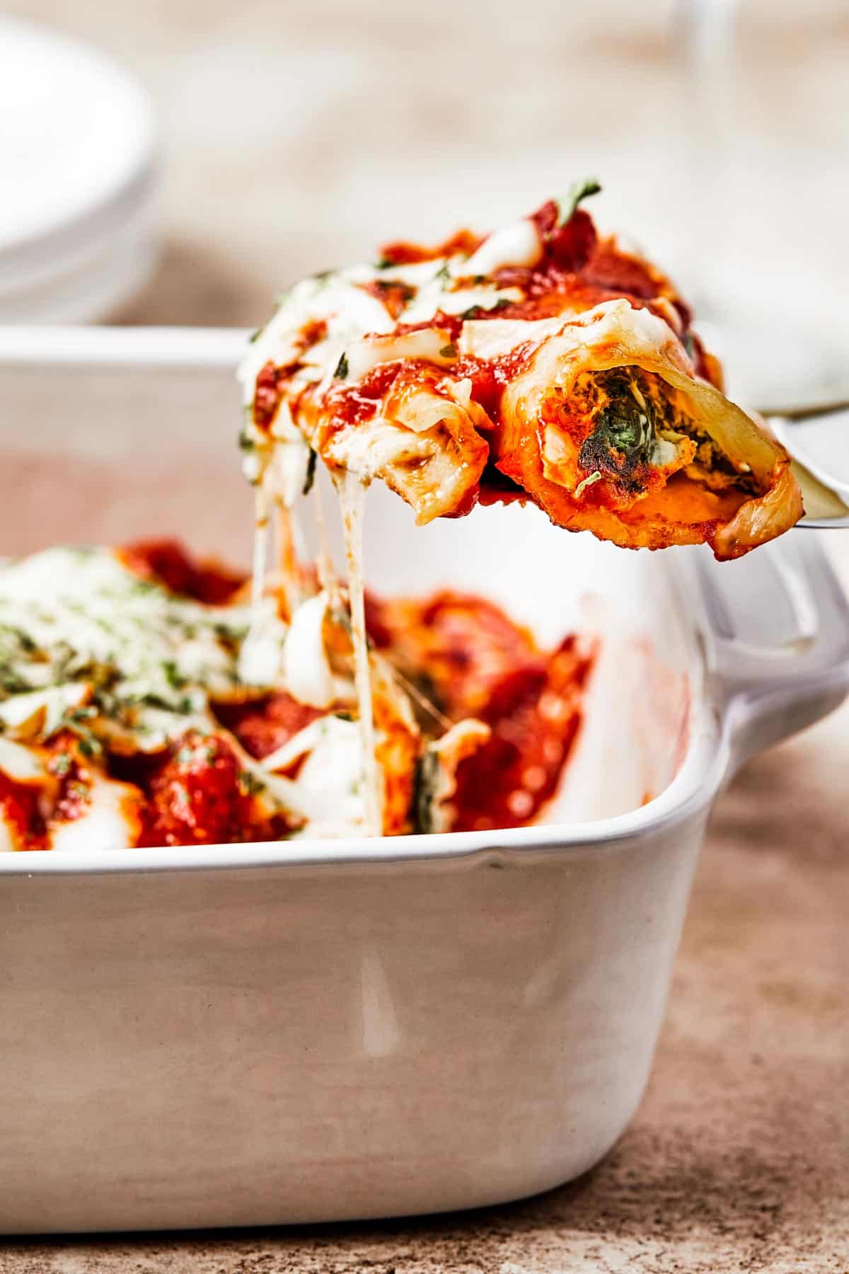 A serving of cheese manicotti being lifted from a casserole dish on a spatula.