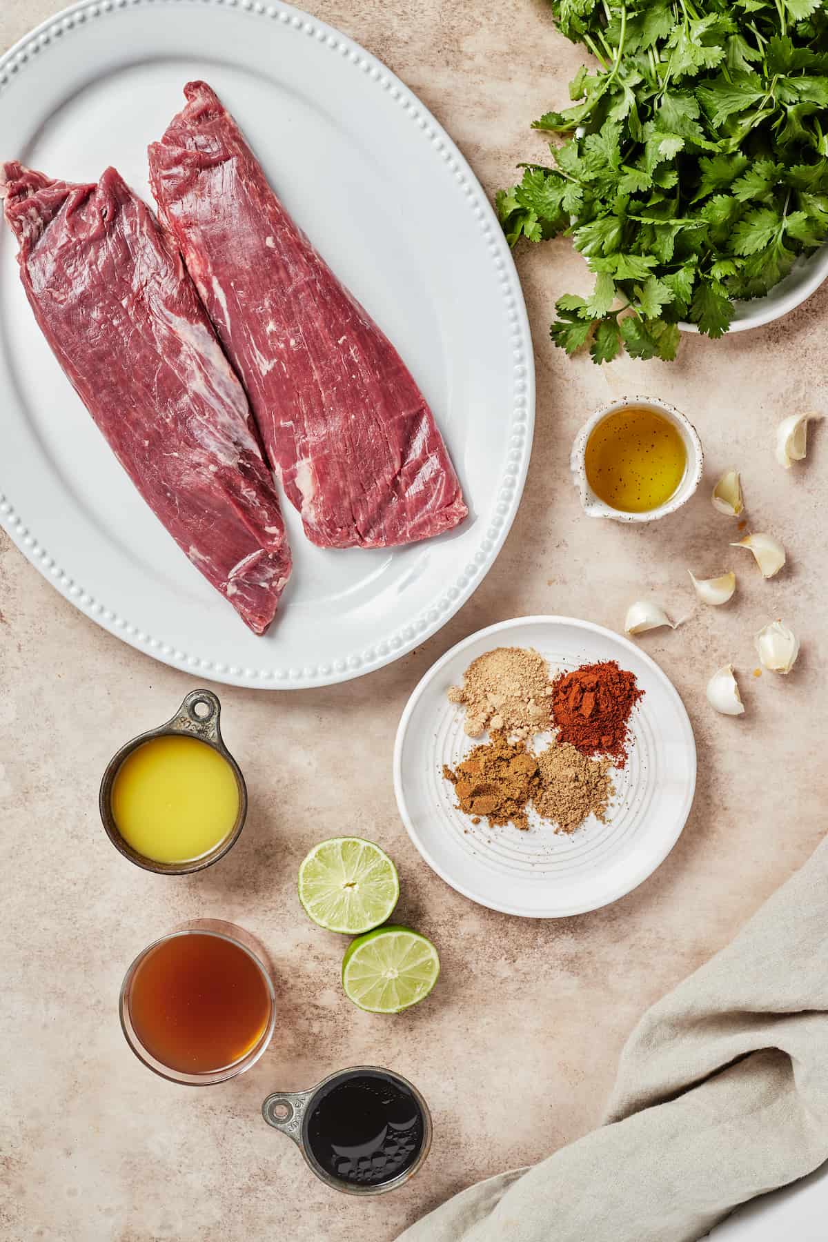 From top left: Flank steak pieces, fresh cilantro, avocado oil, garlic, spices, lime halves, tamari sauce, beef broth, orange juice.