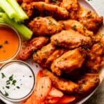 overhead shot of Mango Habanero Hot Wings arranged on a white serving plate with celery sticks and carrots set alongside the wings. Two Jars of hot sauce and ranch dipping sauce are also set on the plate.