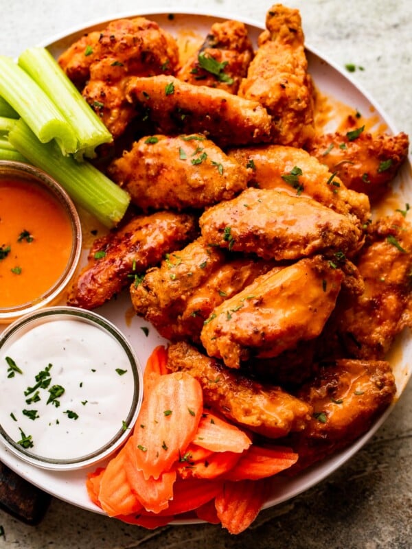 overhead shot of Mango Habanero Hot Wings arranged on a white serving plate with celery sticks and carrots set alongside the wings. Two Jars of hot sauce and ranch dipping sauce are also set on the plate.
