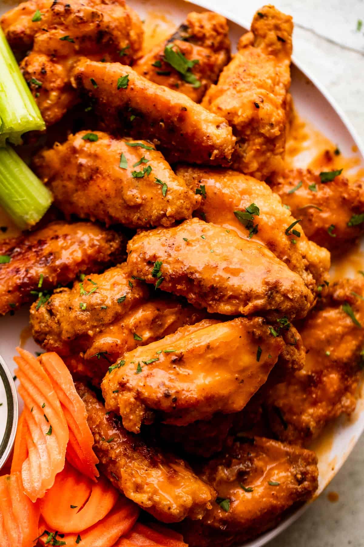 close up overhead shot of Mango Habanero Hot Wings arranged on a white serving plate with celery sticks and carrots set alongside the wings.